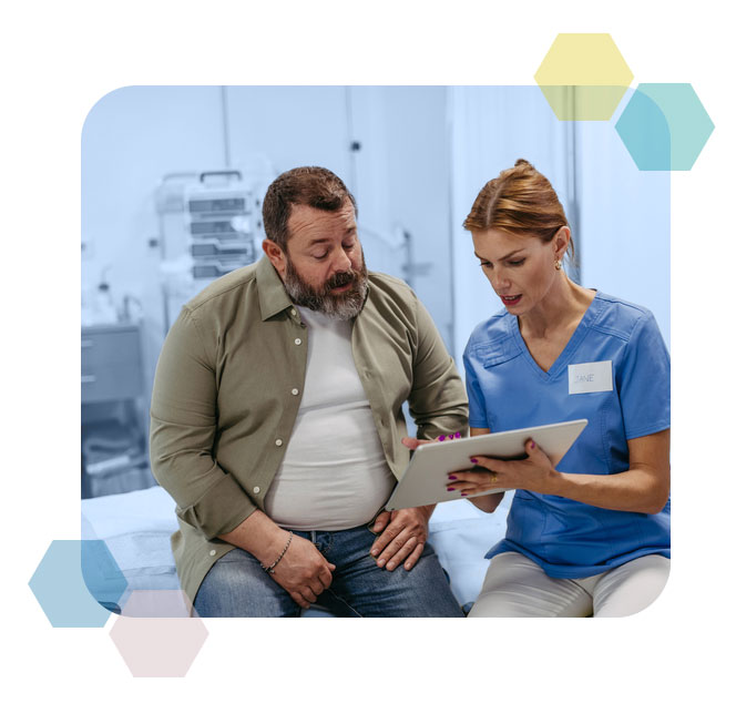Overweight, middle-aged, white man in a button-down shirt sitting with younger, white female doctor looking at an ipad in a medical office. Decorative, brand colored polygons around the outside of the shape, which also has slightly curved edges.